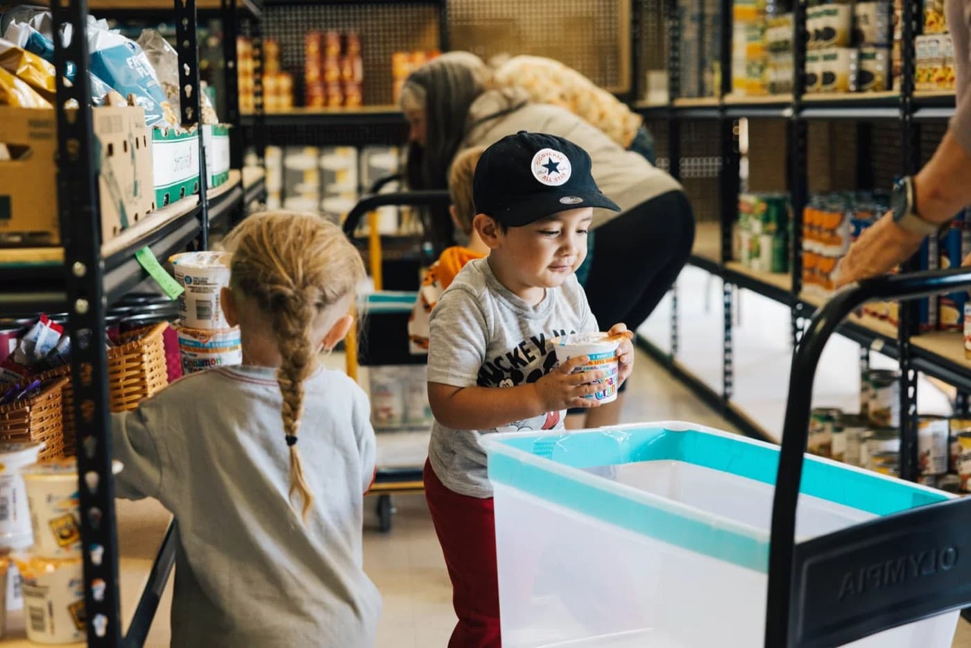 Two young children helping load a family's groceries at the pantry