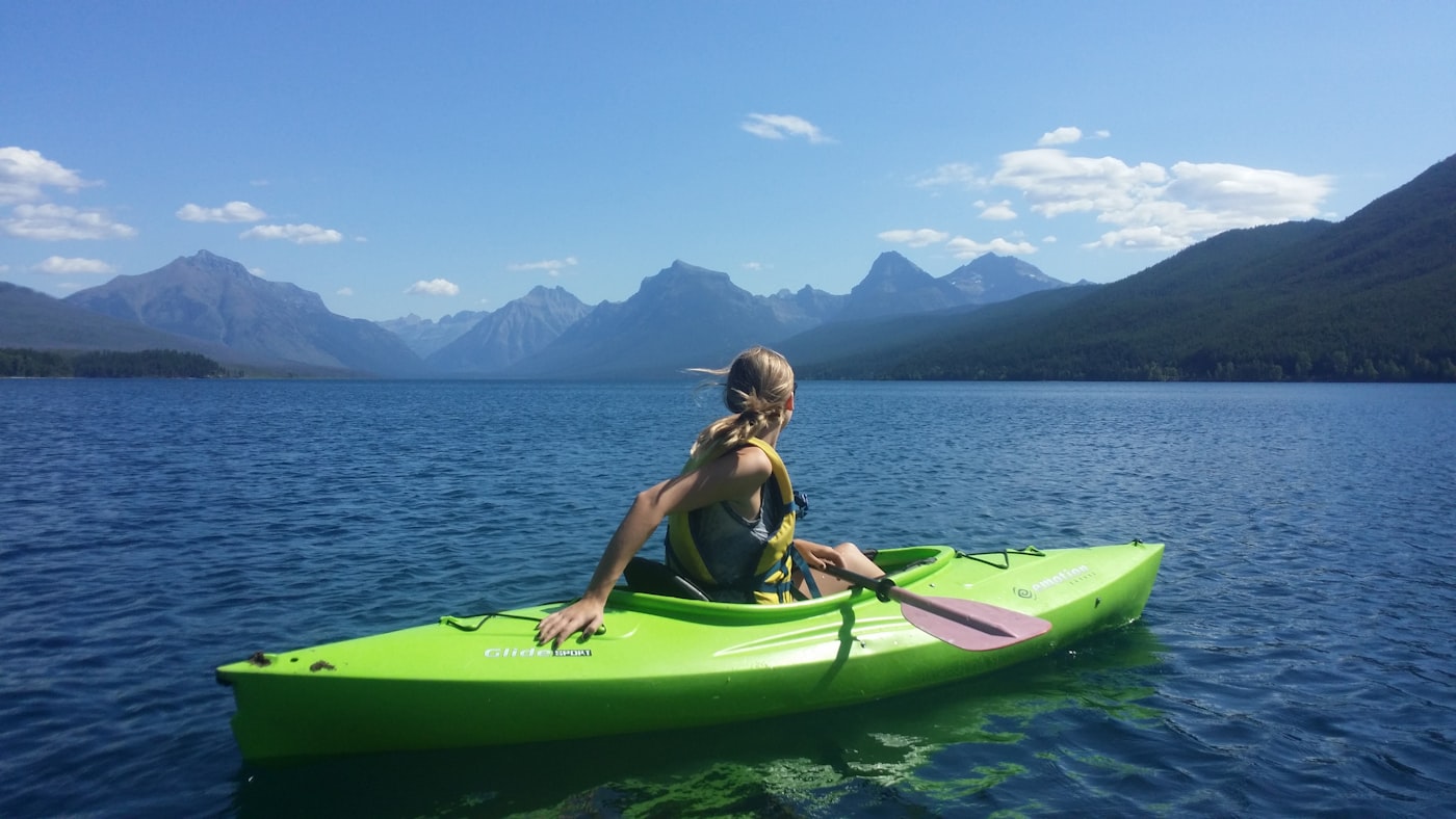 A woman kayaking on a calm alpine lake ringed by mountains