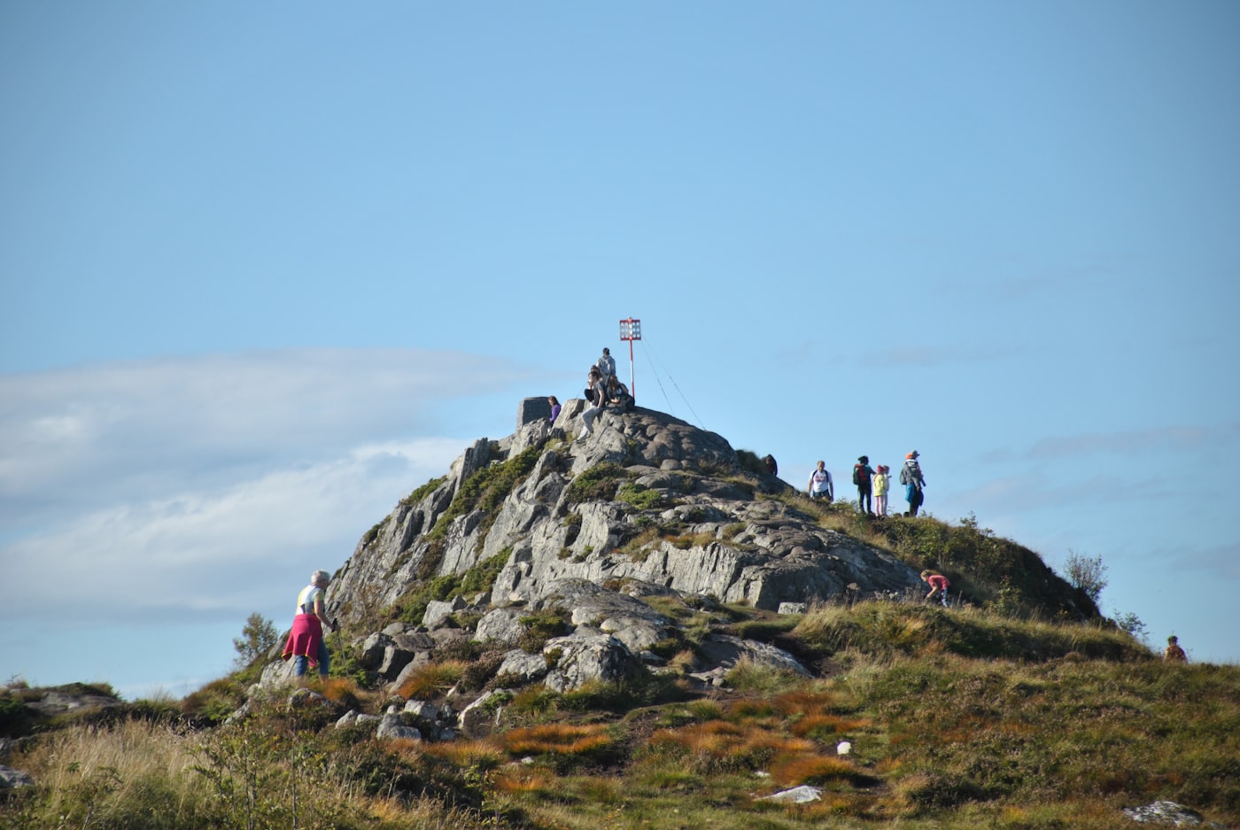 Hikers reaching the top of a rocky mountain peak under a clear blue sky
