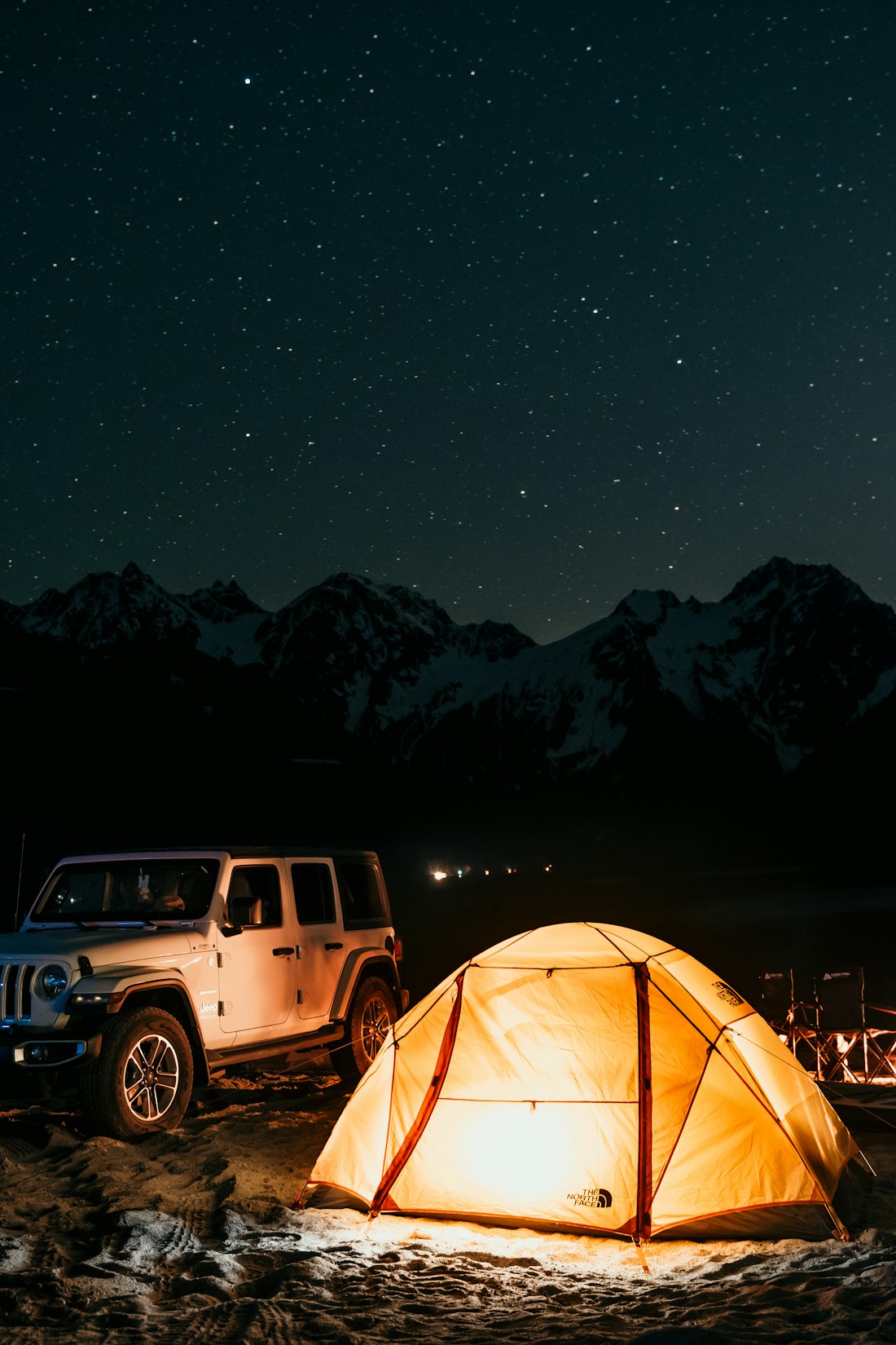A lit tent under a starry night sky with snow-capped peaks
